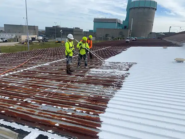 Engelmann Construction workers installing a white liquid applied roof coating on an old, rusty metal commercial roof